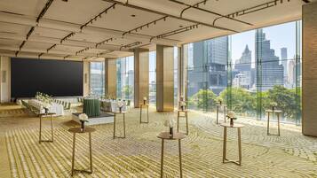 Een ruime hotellobby met grote ramen, een podium en tafels met bloemdecoraties.