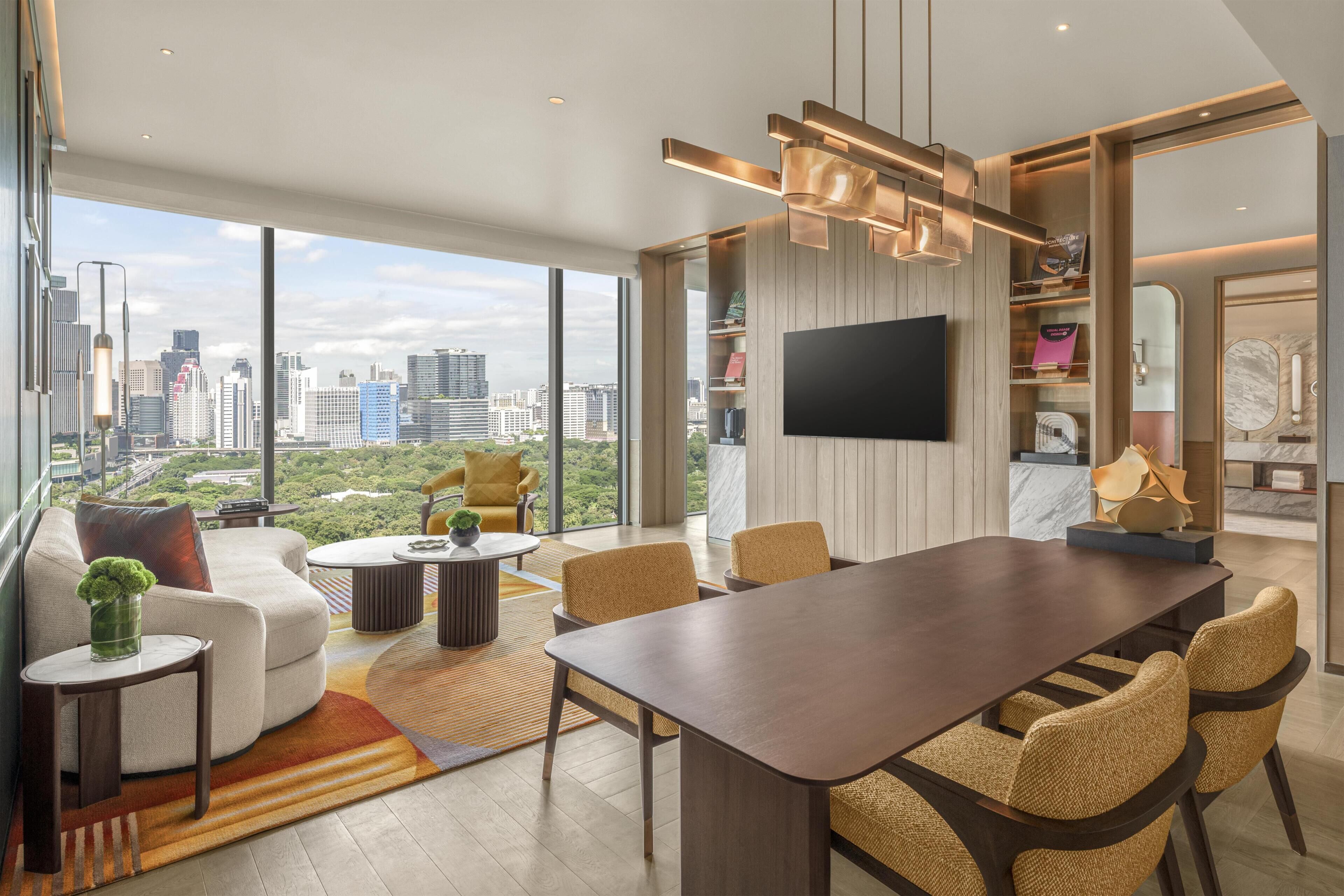 A modern living room with a large dining table, comfortable seating, a flat-screen TV, and a city view.