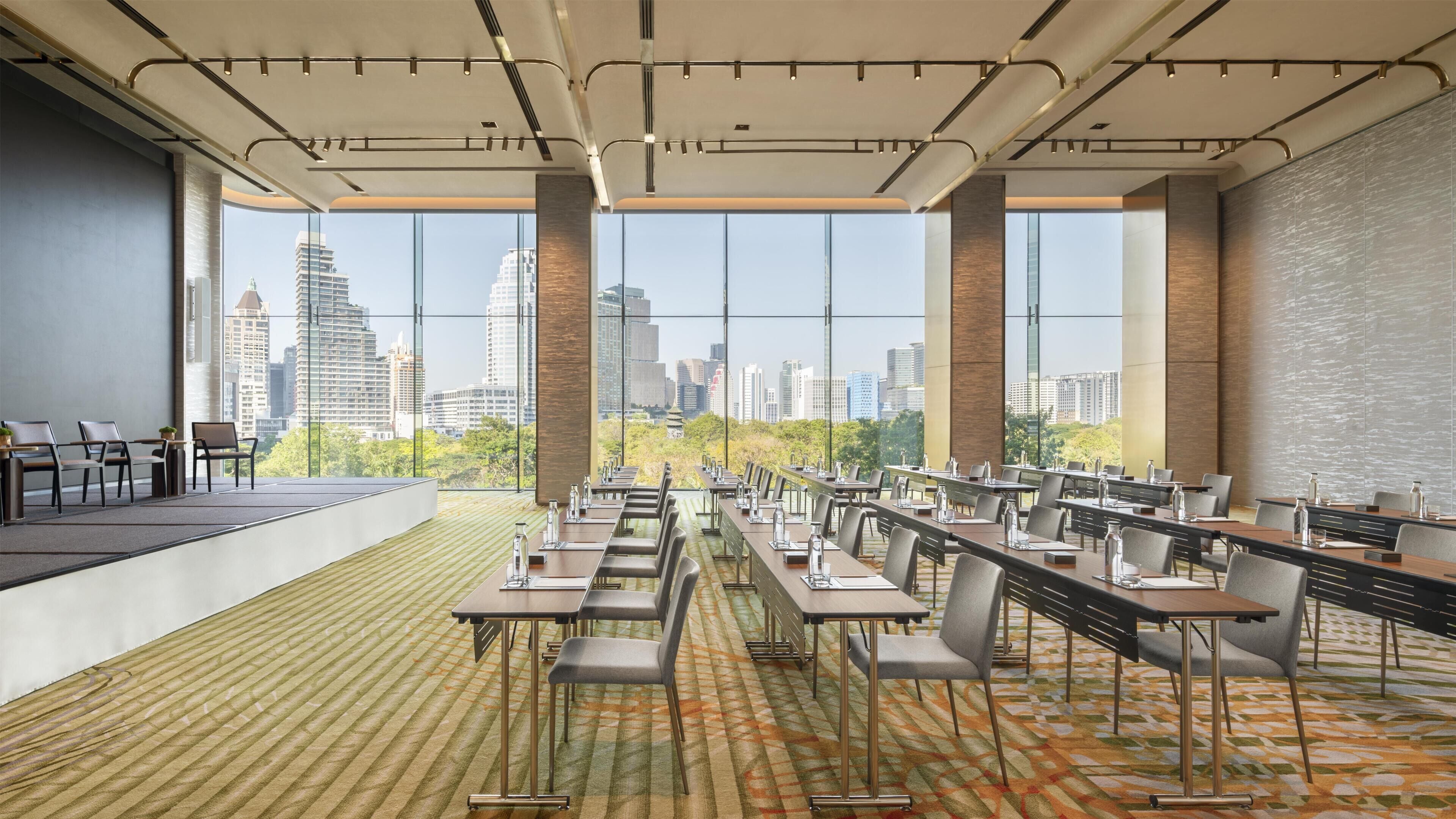 Une salle de conférence équipée de tables et de chaises, de grandes fenêtres donnant sur la ville et d’une scène.