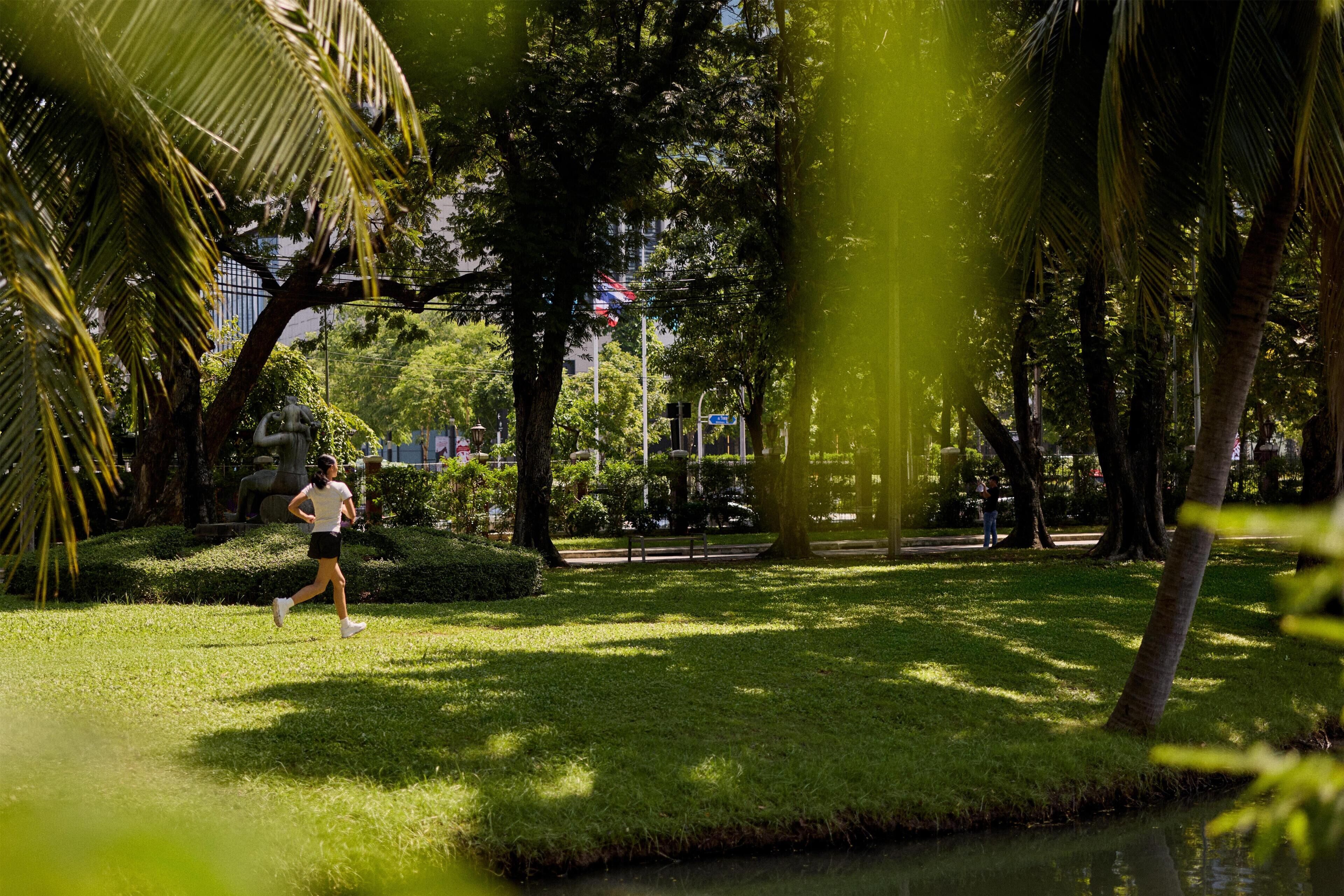 Un parque con un sendero para correr, árboles y una estatua.