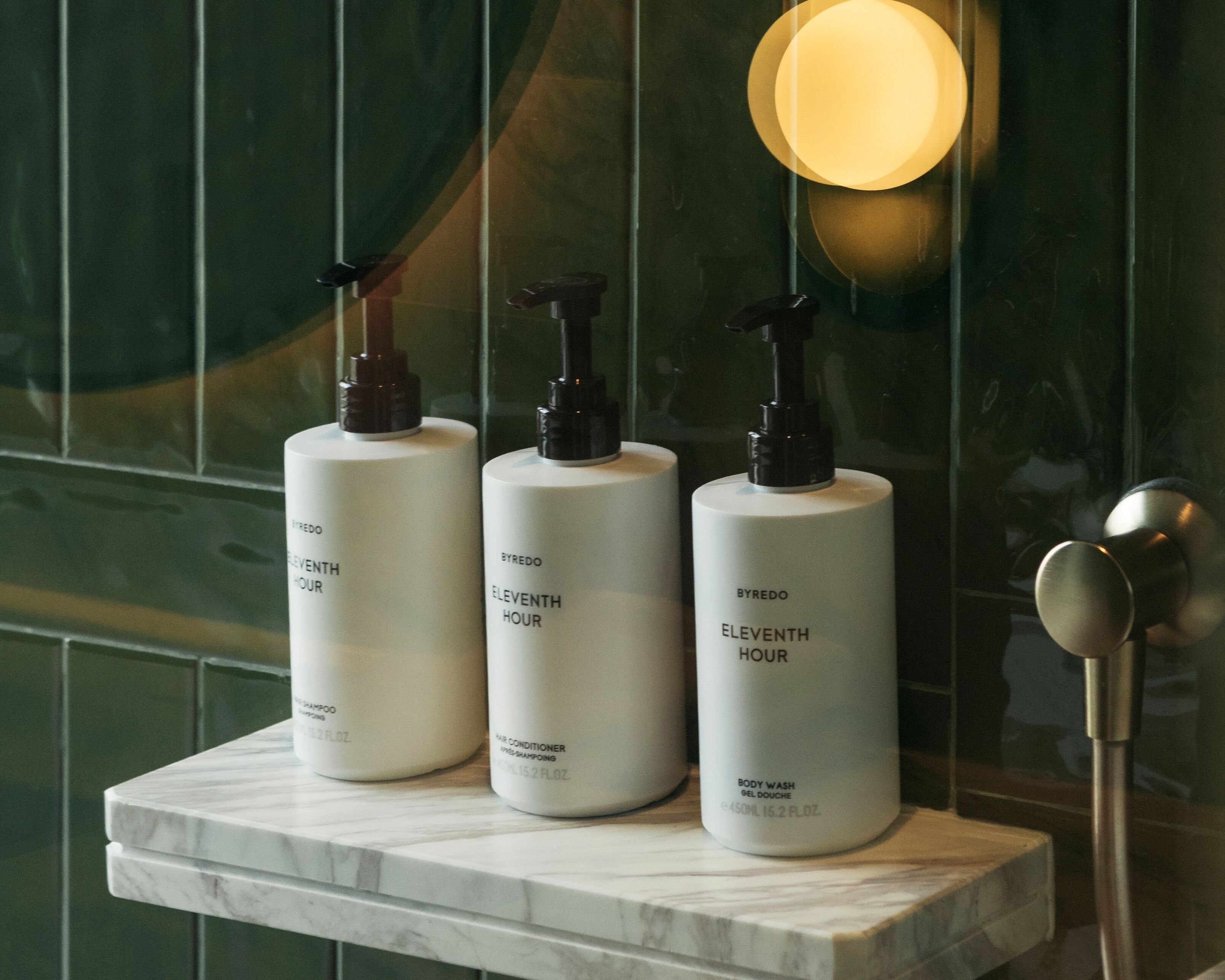 Three bottles of Byredo Eleventh Hour body wash on a marble countertop.