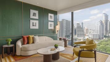 Una sala de estar moderna con sofá, sillón, mesa de centro y vistas a la ciudad a través de amplios ventanales.