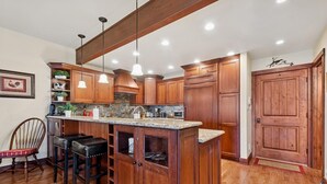 Una cocina con armarios de madera, encimera de granito, iluminación colgante y una isla integrada con taburetes de bar.