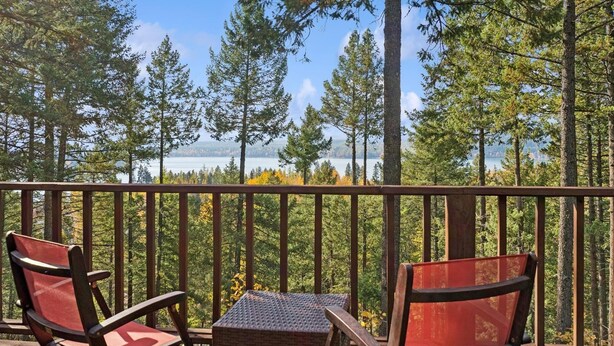 Terraza con dos sillas y una mesa pequeña, con vista a un bosque y un lago.