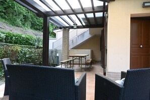 Un patio al aire libre con mobiliario de mimbre, una mesa de madera y una escalera que conduce a un nivel superior.