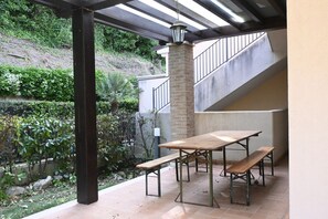 Un patio al aire libre con una mesa, bancos, un pilar de ladrillo y una escalera.