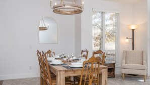 A dining room with a wooden table set for six, surrounded by wooden chairs. A chandelier hangs above, and a mirror is mounted on the wall. - Walk to Skiing, Dining and Downtown (Ketchum)