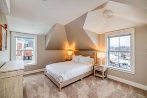 Ein Schlafzimmer mit einem Bett, zwei Nachttischen, einer Kommode und großen Fenstern mit Blick.