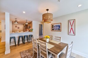 Un espace repas avec une table en bois, des chaises blanches et un lustre.