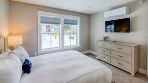 A bedroom with a bed, a dresser, a TV, and a window with a view of the outside. - Cady Suite at 109 Main (Stowe)