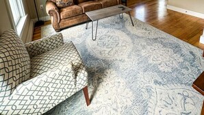 A spacious living room with a brown leather sofa, patterned cushions, a light-colored coffee table, and a large patterned rug. - Pinnacle Suite at 109 Main (Stowe)