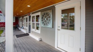 A covered porch with a wooden ceiling, a white door, and a large clock on the wall. - Pinnacle Suite at 109 Main (Stowe)