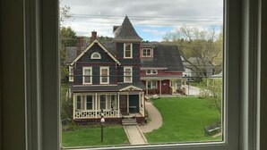 A window with a view of a two-story house with a porch and a lawn. - Sterling Suite at 109 Main (Stowe)