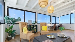 A spacious living area with large windows, a dark coffee table, and two beige armchairs with yellow cushions. - Vacation Home 'Esencia House Bajo Las Estrellas' with Mountain View, Private Pool and Wi-Fi (Puerto del Rosario)