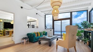 A spacious living area with a large window, a green sofa, a coffee table, and a beige armchair. - Vacation Home 'Esencia House Bajo Las Estrellas' with Mountain View, Private Pool and Wi-Fi (Puerto del Rosario)