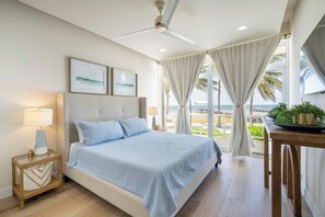 A bedroom with a bed, a nightstand, a lamp, a ceiling fan, and a view of the beach. - Styles Beach 1A - Beachfront Luxury Condo w/ Pool (San Pedro Town)