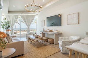 A spacious living room with a view of the beach, a large chandelier, and modern decor. - Styles Beach 1A - Beachfront Luxury Condo w/ Pool (San Pedro Town)