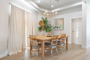 A dining area with a wooden table and wicker chairs, a chandelier, and a potted plant. - Styles Beach 1A - Beachfront Luxury Condo w/ Pool (San Pedro Town)
