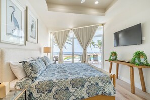 Een slaapkamer met een groot bed, een televisie en uitzicht op het strand.