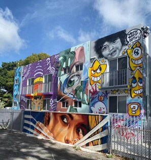 A building with colorful murals and graffiti, featuring various characters and faces. - Prime Location | Free Parking |By Nightlife & Eats (Miami)