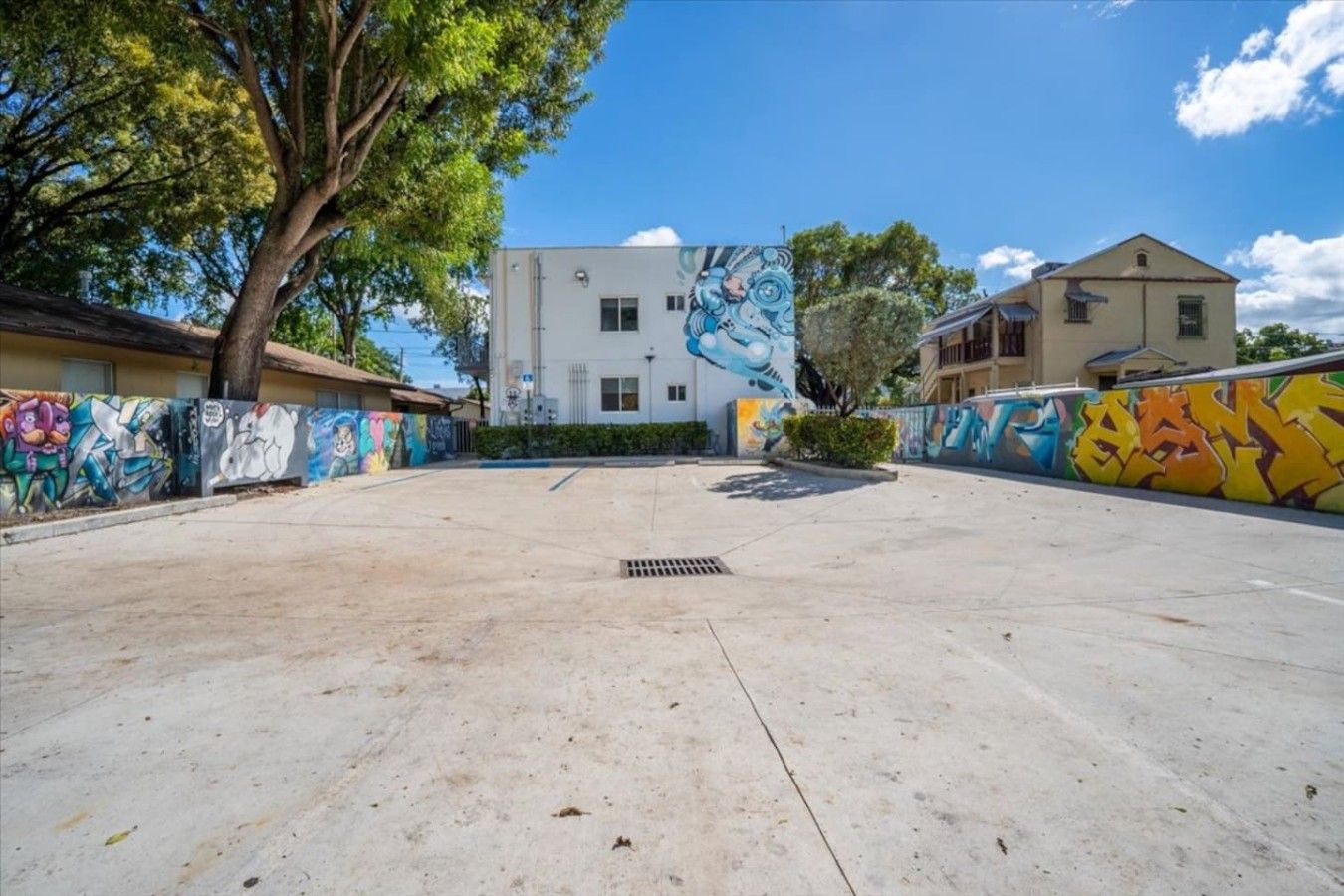 An outdoor courtyard with a concrete floor, surrounded by buildings with colorful graffiti on the walls.