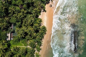 An aerial view of a beach with palm trees, a sandy shore, and a rocky outcrop. - Sama Retreats (Galle)