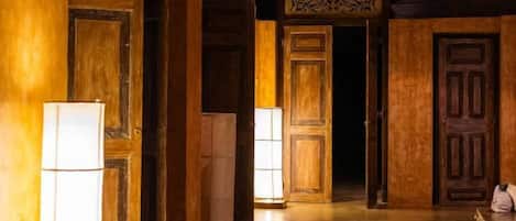 A corridor with wooden doors and walls, a patterned ceiling, and a floor that appears to be made of wood or a wood-like material.