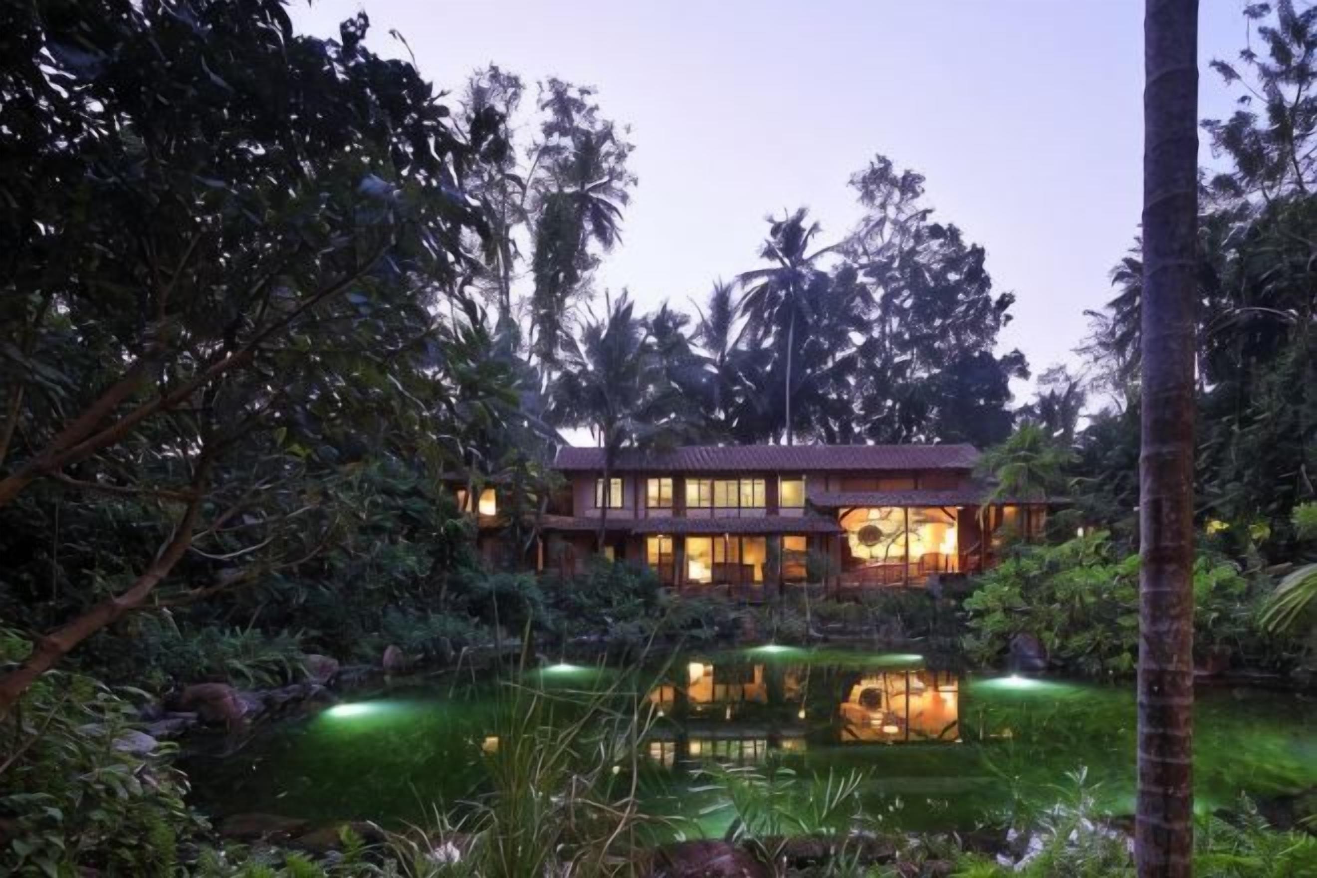 Um edifício de dois andares com um lago espelhado na frente, cercado por vegetação tropical exuberante.