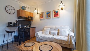 A compact living space with a kitchenette, a sofa, two round tables, and wall-mounted artwork.