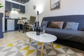 A modern living room with a sofa, a dining table, and a kitchen area. - Le Cocoon de Belle Hutte sous les sapins (La Bresse)