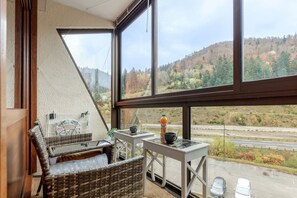 Une pièce avec une grande fenêtre, des meubles en osier, une petite table et une bouteille de jus d’orange.