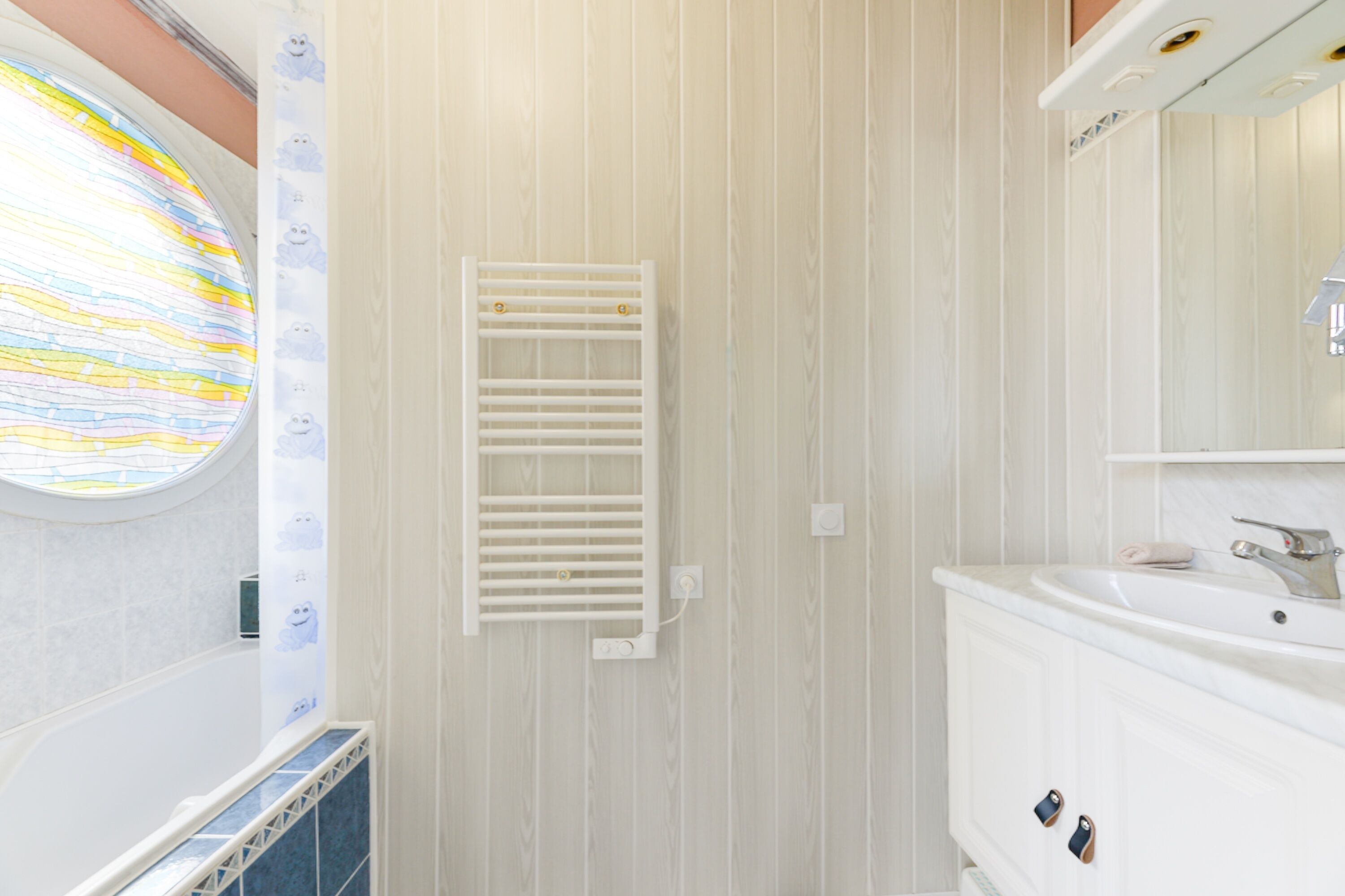 Ein Badezimmer mit einer Badewanne, einem weißen Waschbecken und einem Fenster mit Streifenmuster.