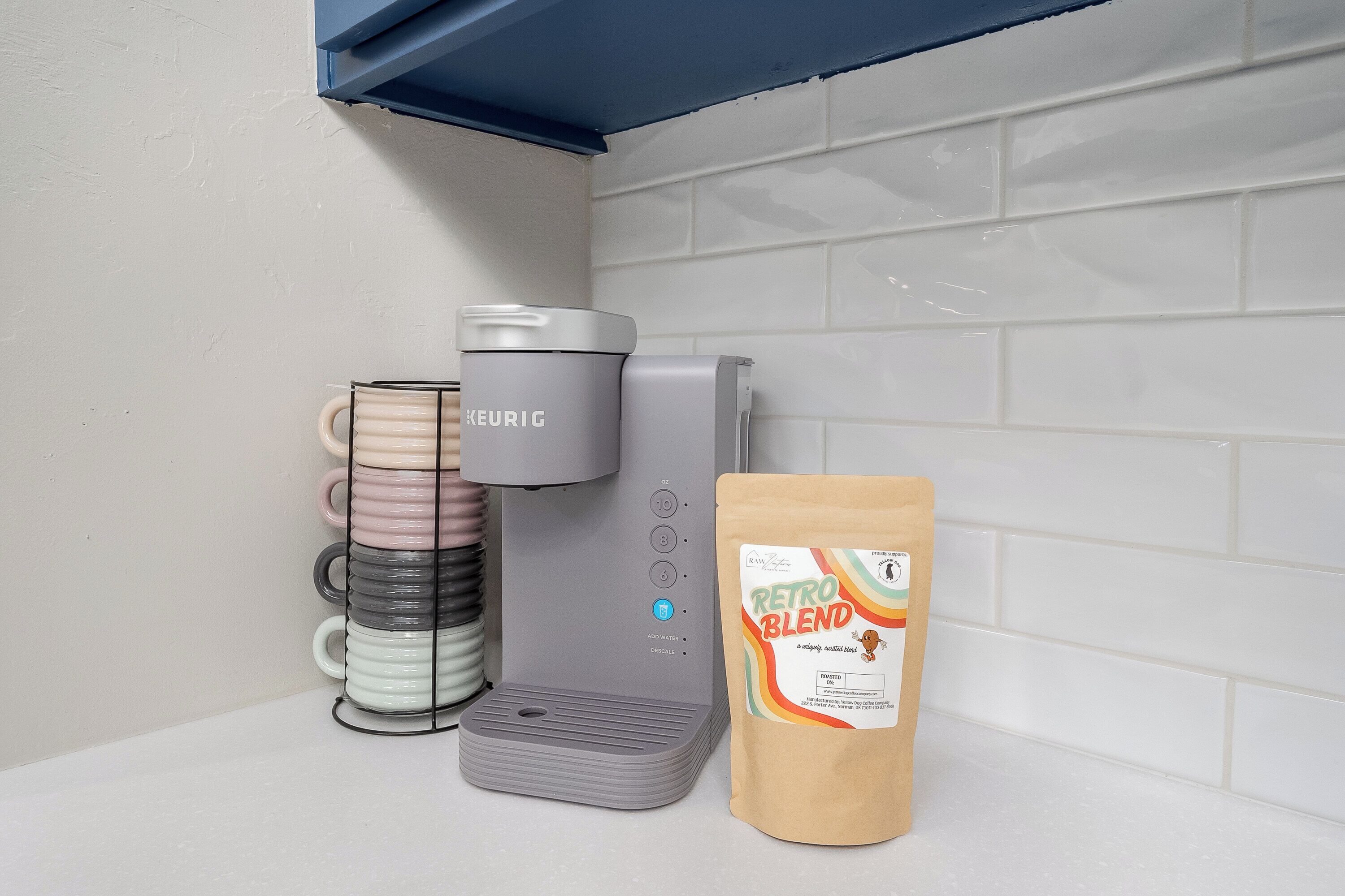 Eine Kaffeemaschine von Keurig, ein Vorratshalter für Kaffeekapseln und eine Packung Retro Blend Kaffee.