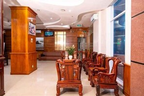 Et hotellobby med møbler i træ, en receptionsdisk og et fjernsyn.