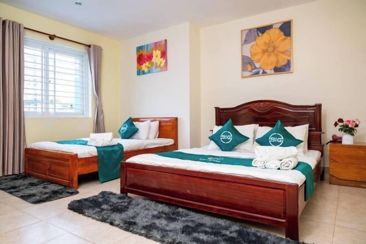 Een hotelkamer met twee houten bedden, een groot raam met gordijnen en kunst aan de muur.
