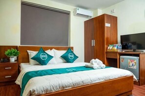 Une chambre d’hôtel comprenant un lit, un bureau avec une télévision, un petit réfrigérateur et une armoire.