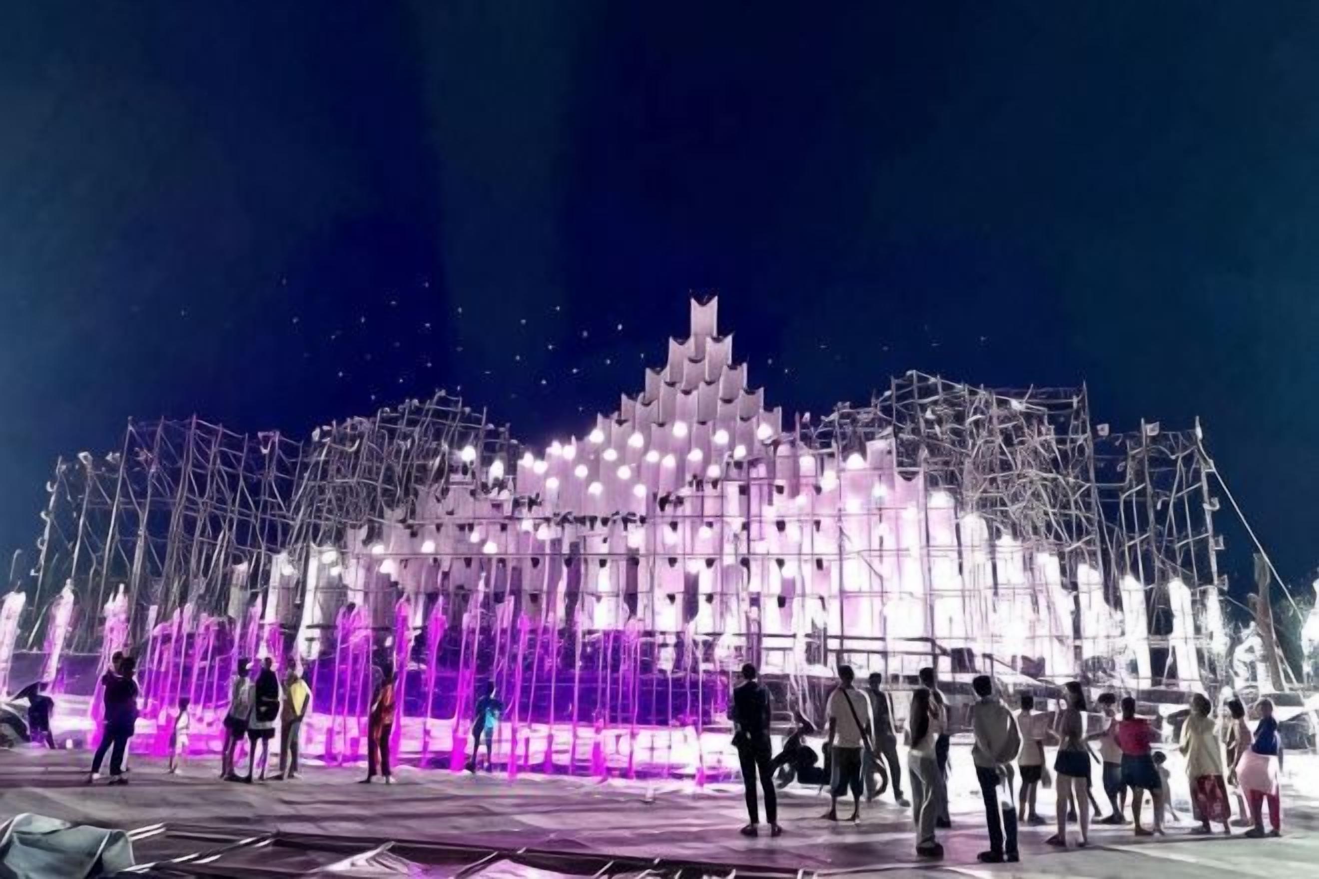 Una estructura grande e iluminada con un diseño escalonado, rodeada por una multitud de personas.