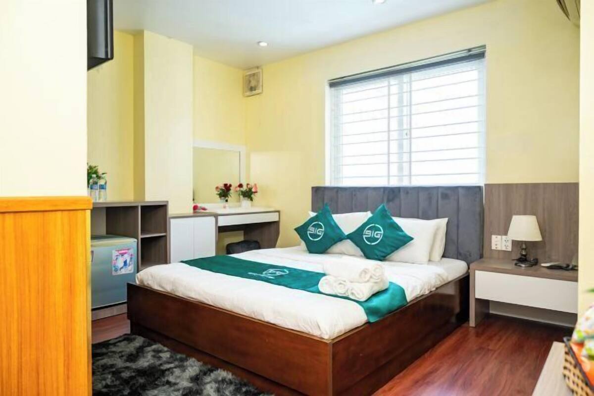 Een hotelkamer met een bed, nachtkastje, bureau en een raam met jaloezieën.