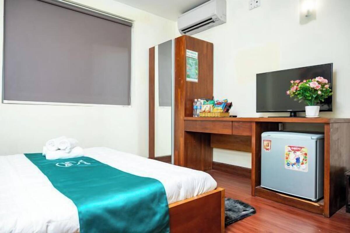 Een hotelkamer met een bed, een bureau met een televisie, een kleine koelkast en een raam met een blind.
