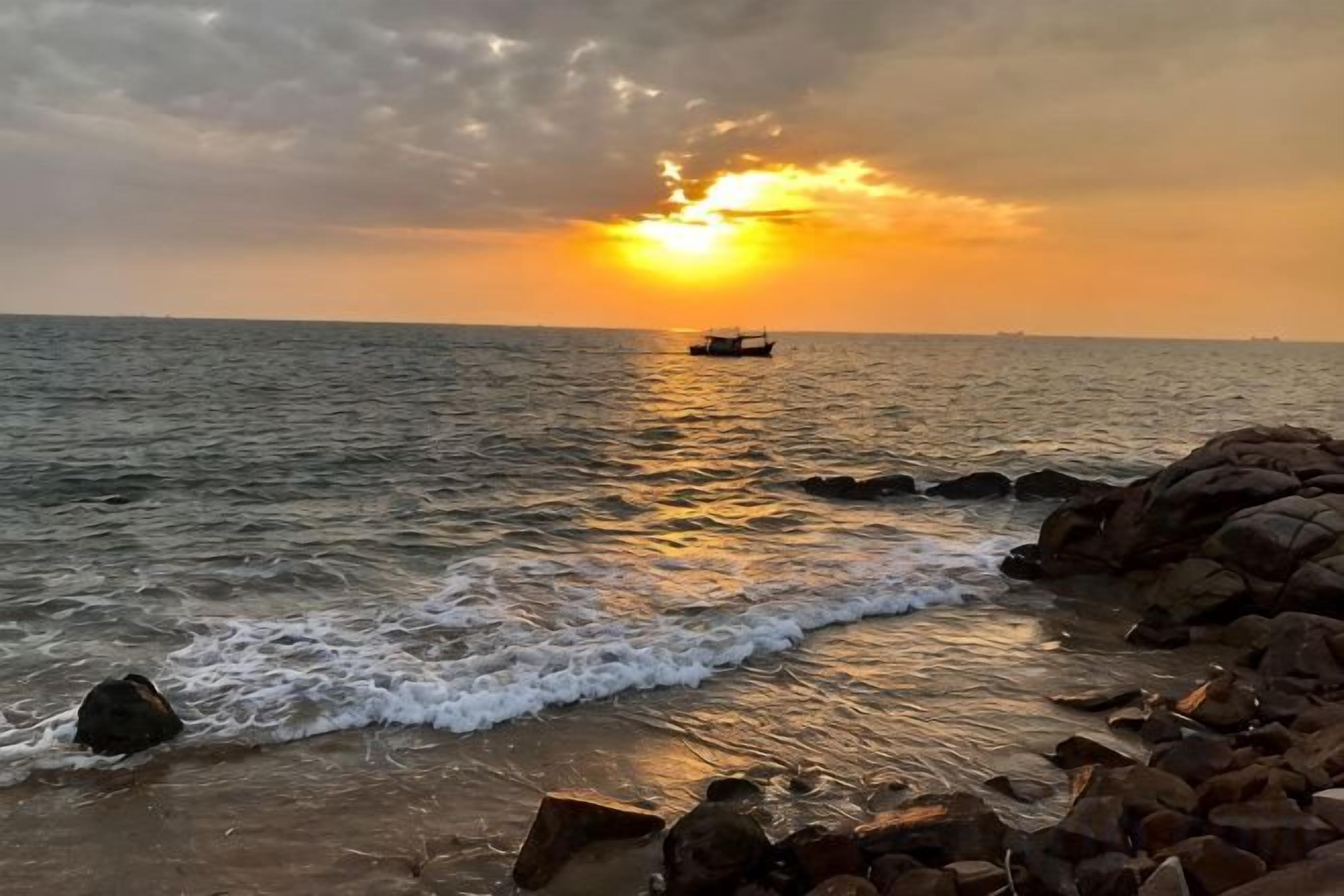 Ein Sonnenuntergang über dem Meer mit einem Schiff in der Ferne und einer felsigen Küstenlinie.