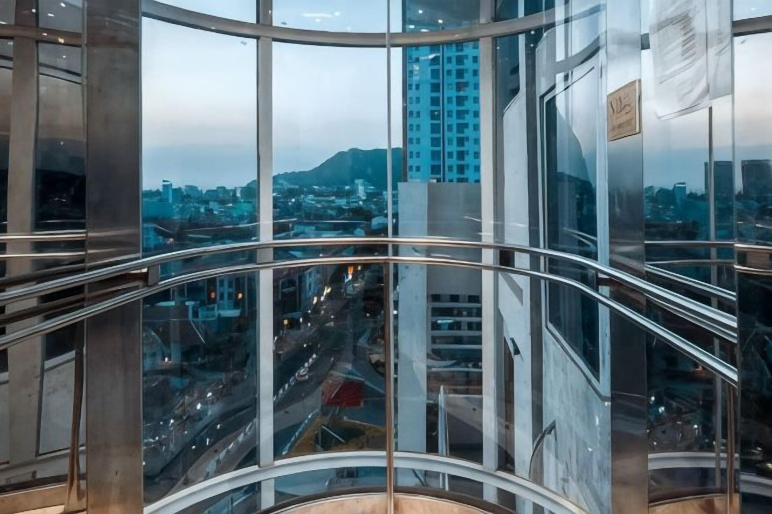 Un edificio moderno con barandillas de vidrio curvo y vista a un paisaje urbano.