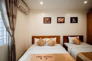 Une chambre d’hôtel avec deux lits, une fenêtre avec des rideaux et trois tableaux encadrés accrochés au mur.