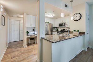 A modern kitchen with white cabinets, stainless steel appliances, a granite countertop, pendant lighting, and a wall clock. - Luxurious 2 -Bedroom Apartment: King Bed + Private Garage (Roseville)