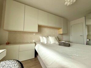 Quarto moderno com cama grande, armários embutidos, mesa de cabeceira e uma cadeira.