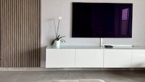 Ein modernes Wohnzimmer mit flachbildfernseher an der Wand, einer weißen Unterhaltungseinheit darunter und einem großen beigefarbenen Sofa.