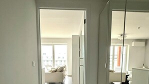 Eine moderne Wohnung mit minimalistischem Design, ausgestattet mit einem großen Spiegel, einer Bank und Blick auf die Stadt durch die Fenster.
