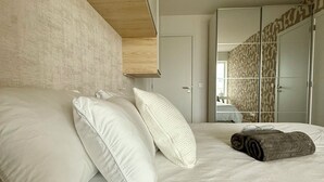 Ein modernes Schlafzimmer mit einem großen Bett, weißen Kissen, einem aufgerollten Handtuch und einer Holzbalkendecke.