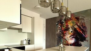 Eine moderne Küche mit einer weißen Kochinsel, Pendelleuchten und einem farbenfrohen abstrakten Gemälde an der Wand.