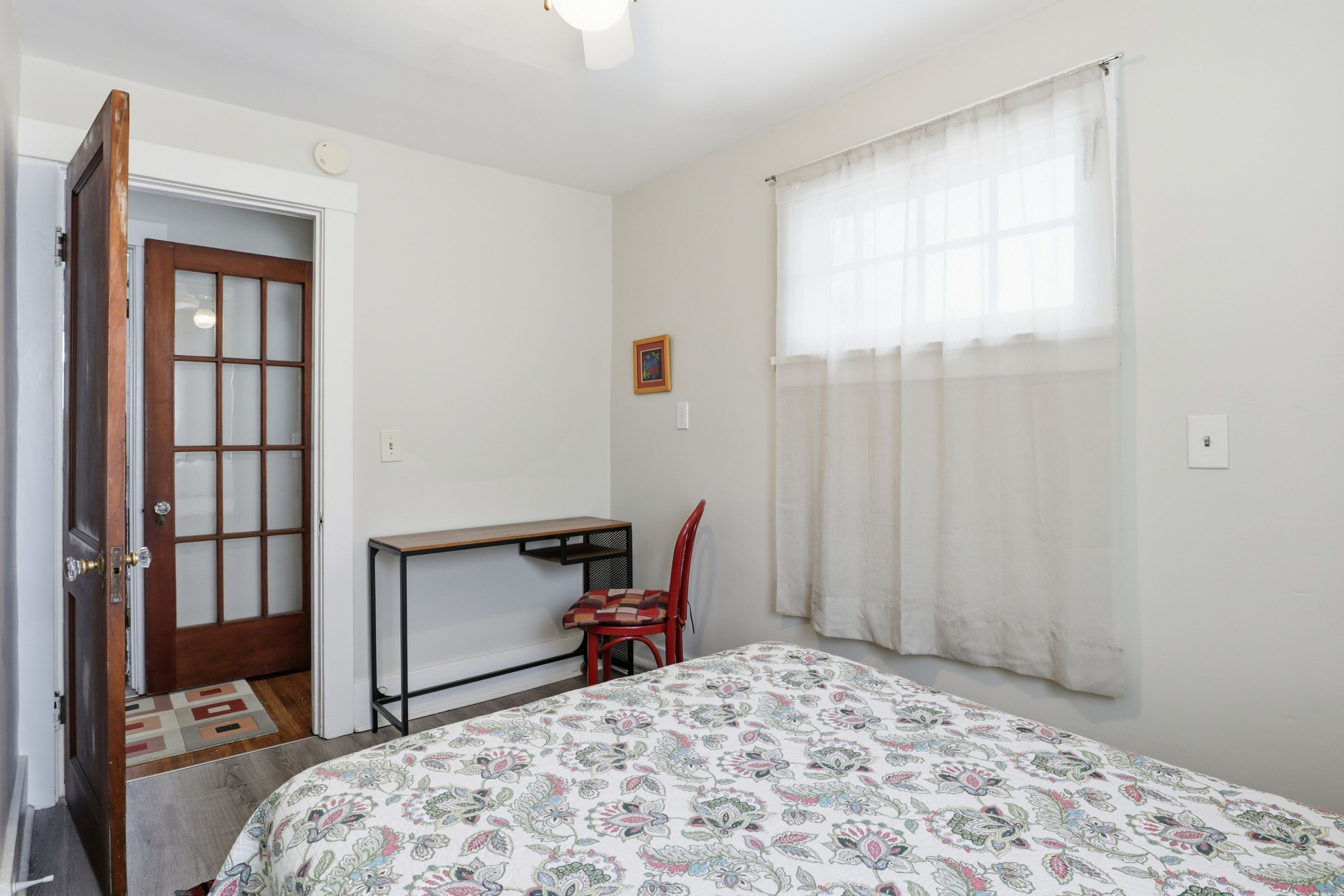 A bedroom with a bed, a desk, a chair, a door, and a window with curtains.