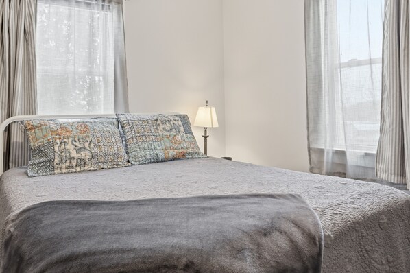 A bedroom with a bed, pillows, a lamp, and sheer curtains.